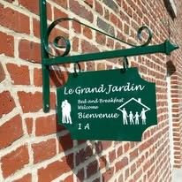 Willkommen im Le Grand Jardin, einer Fruehstueckspension in Neufchateau, Ardennen, mit einem attraktiven Schild an einer Backsteinmauer.