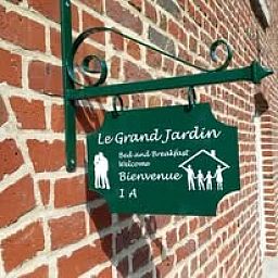 Willkommen im Le Grand Jardin, einer Fruehstueckspension in Neufchateau, Ardennen, mit einem attraktiven Schild an einer Backsteinmauer.